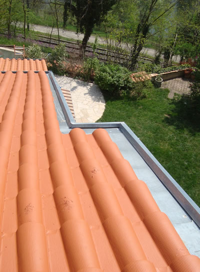 Rénovation de toiture en tuiles orange et zinguerie Toiture en tuiles terre cuite orange avec finitions en zinguerie et vue sur un jardin arboré.