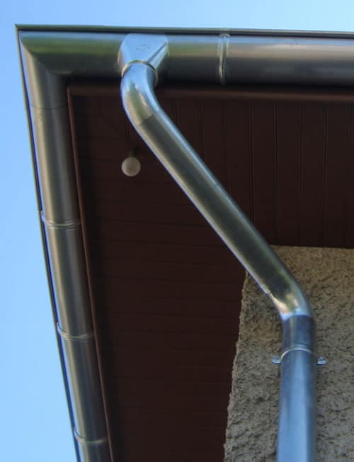 Installation Gouttière Zinc et Descente d'Eau Pluviale Gouttière en zinc et descente pluviale installées sous l'avant-toit d'une maison avec mur en crépi.