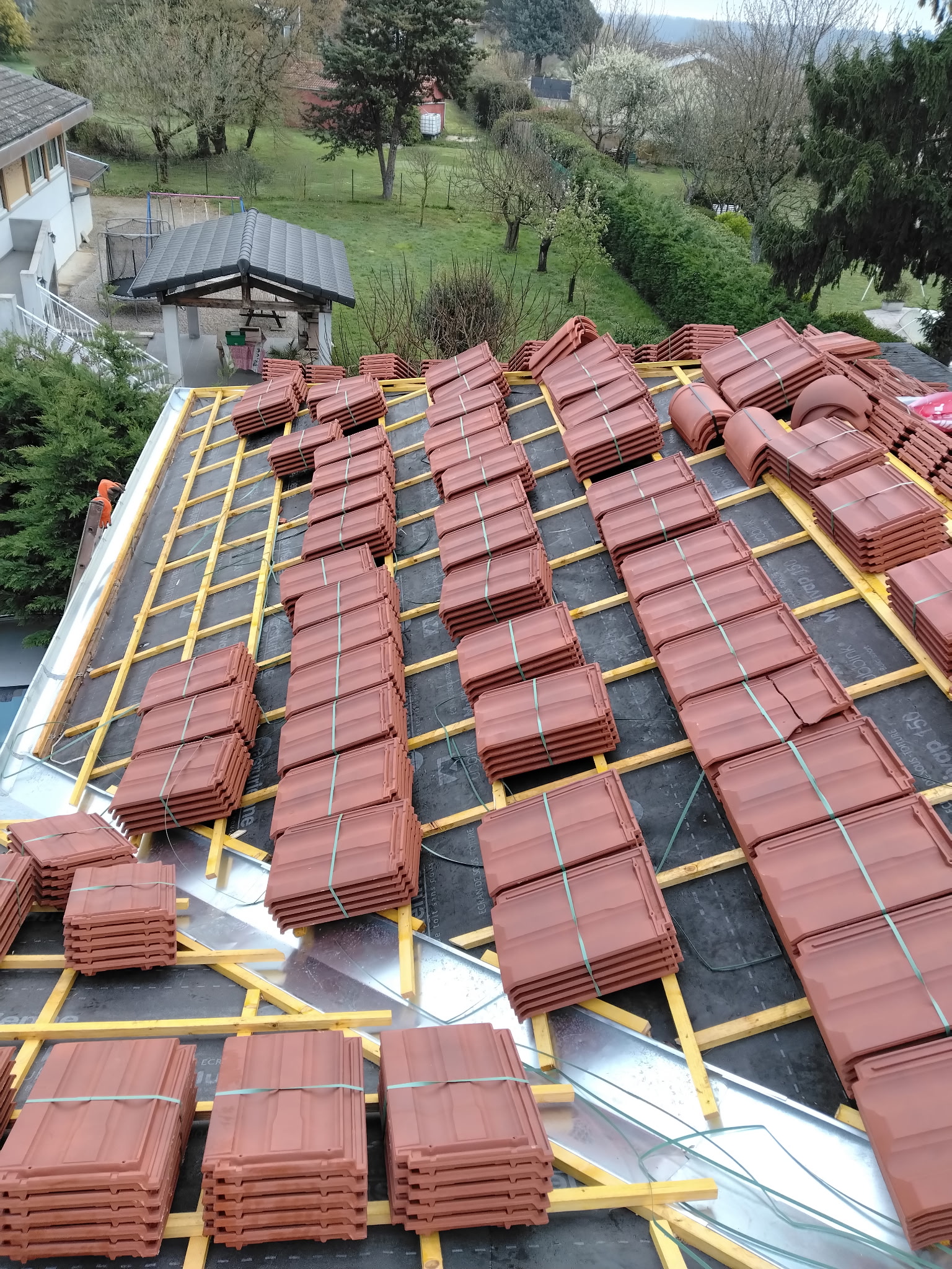 Rénovation de Toiture : Pose de Tuiles en Terre Cuite Tuiles en terre cuite rouge empilées sur liteaux en bois pour la rénovation d'une toiture inclinée.