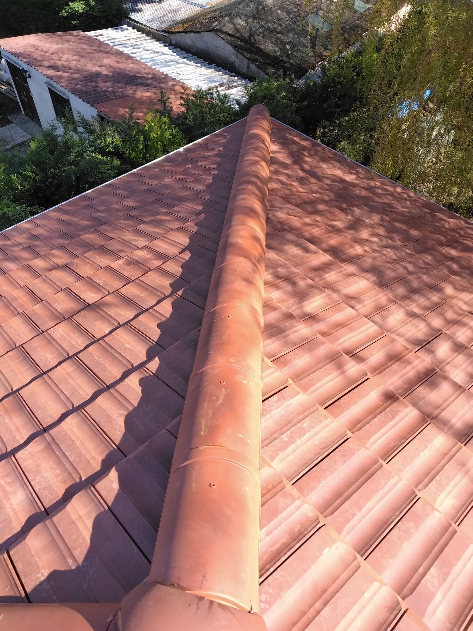 Toiture en tuiles de terre cuite : zoom sur le faitage Toiture en tuiles de terre cuite rouge avec un faîtage central impeccable sous la lumière du soleil.