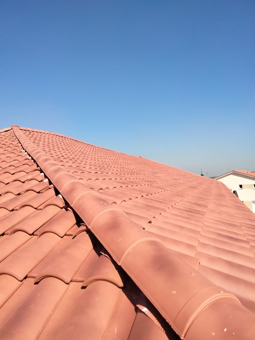 Toiture en Tuiles de Terre Cuite : Pose et Finitions Toiture en tuiles de terre cuite rouge avec détail du faîtage sous un ciel bleu.